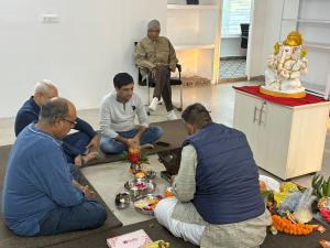 A traditional Ganesh puja being performed during an office inauguration, with a priest conducting rituals and participants seated around ceremonial items and offerings.