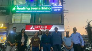 A group of people standing outside the Healthy Jeena Sikho building, with the illuminated signboard showcasing the new Physiotherapy and Sleep Test Center in the background.