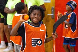 Camper wearing Philadelphia Flyers pinnie holds a hockey ball and stick - as part of a special event at the Coatesville YMCA summer camp.