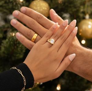 Image showing a man wearing a wedding band and a woman wearing an engagement ring from Modern Gents in front of a Christmas tree