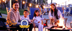 A family enjoys a cozy evening around a campfire, roasting marshmallows, with string lights in a serene outdoor setting.