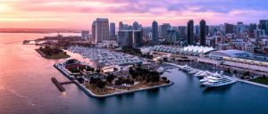 Sunset view of San Diego's harbor, featuring yachts, a marina, the convention center, and a skyline of modern skyscrapers.