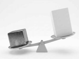 A heavy metal block sinks the scale when weighed against a larger, yet lighter plastic block, underscoring the significant weight savings plastics can offer.