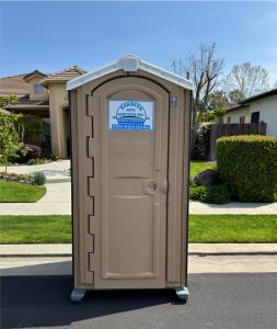 A row of several tan portable toilets on a green grassy field.