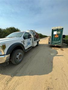 A white Barrios Site Services truck parked next to a green portable toilet on a dirt road in a field